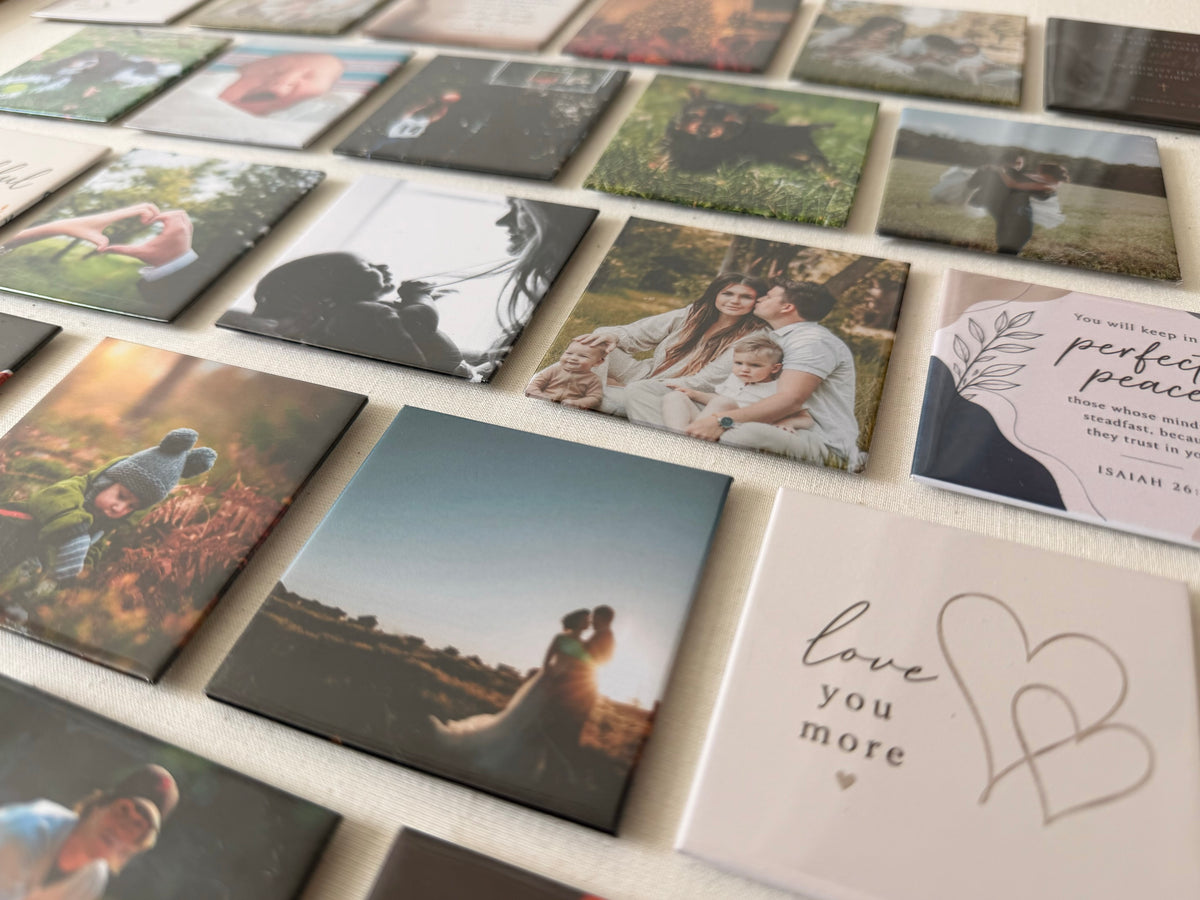 Rows of finished photo magnets laid out on cream linen: family portraits, a dog, a verse magnet and a wedding photograph.