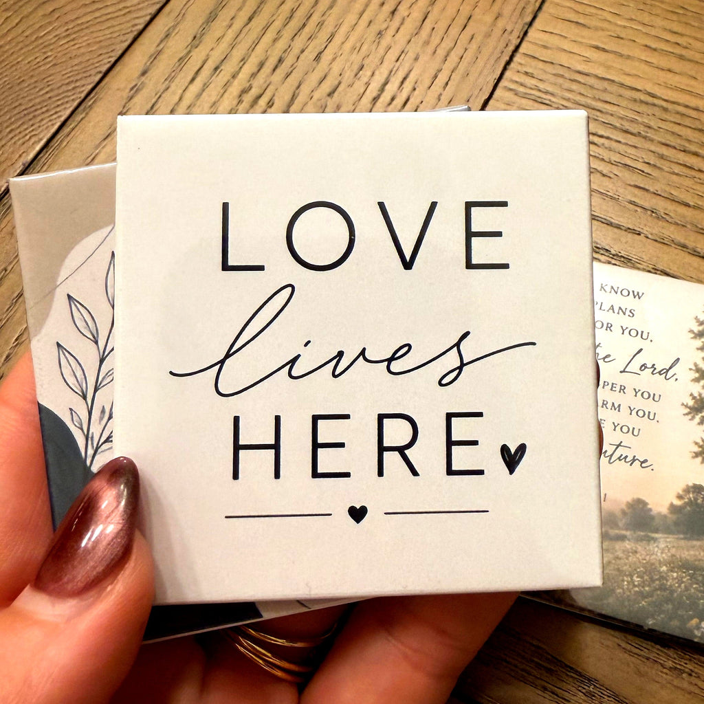 A photo magnet reading Love Lives Here, held in a hand