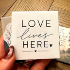 A photo magnet reading Love Lives Here, held in a hand