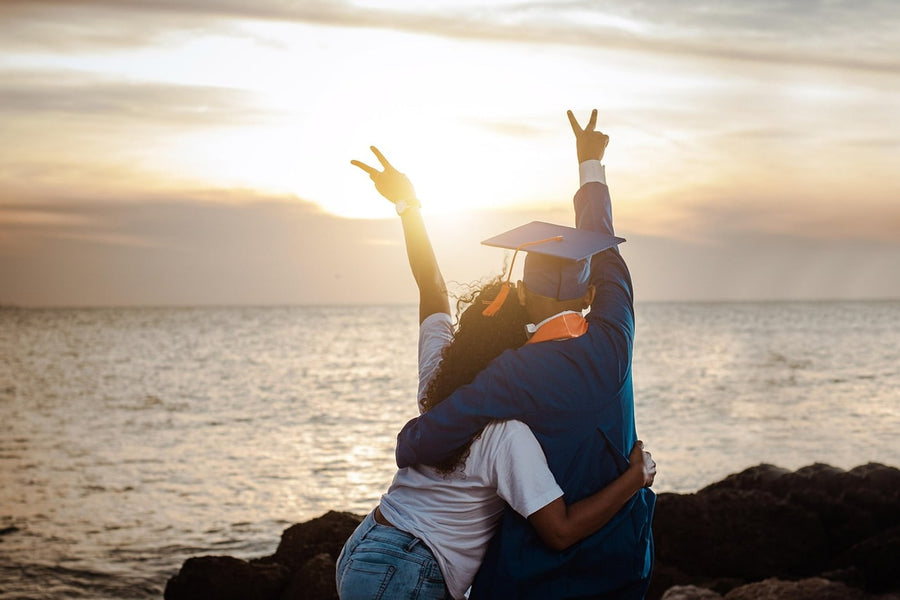Two people embracing at sunset, one wearing a graduation cap